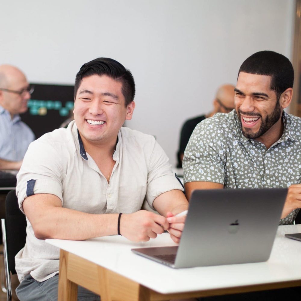 Three male workers share a laugh over work on computers.